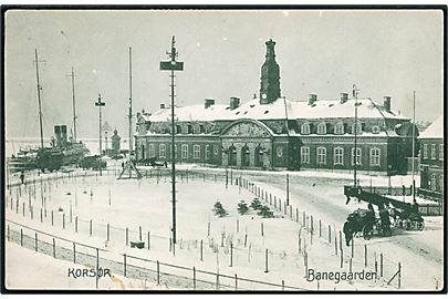 Korsør banegård i sne med dampskib i baggrunden. Stenders no. 19097.