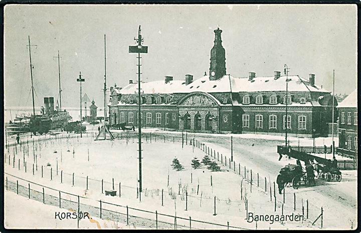 Korsør banegård i sne med dampskib i baggrunden. Stenders no. 19097.