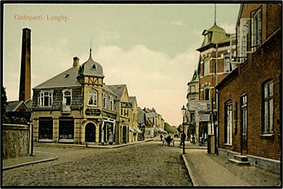 Lyngby, gadeparti med Lyngby ny Colonial - Mel & Gryn Magasin og skilt Baadfarten Lyngby, Frederiksdal, Fiskebæk, Holte. G. M. no. 2558.