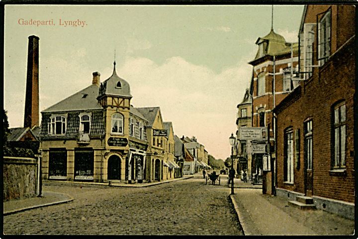 Lyngby, gadeparti med Lyngby ny Colonial - Mel & Gryn Magasin og skilt Baadfarten Lyngby, Frederiksdal, Fiskebæk, Holte. G. M. no. 2558.