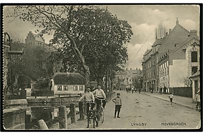 Lyngby, hovedgade med gadekær og kirke i baggrunden. Flensborglagret u/no.