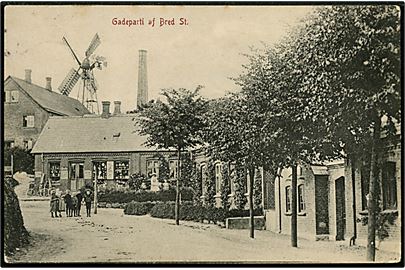 Bred st. Gadeparti med Manufakturhandelen og vindmølle i baggrunden. 