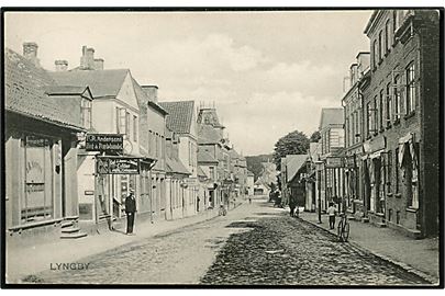 Lyngby. Gadeparti med F.R. Andersens Bog & Papirhandel, Carl J. Jensens Cyklehandler og flere andre. Stenders no. 3793.