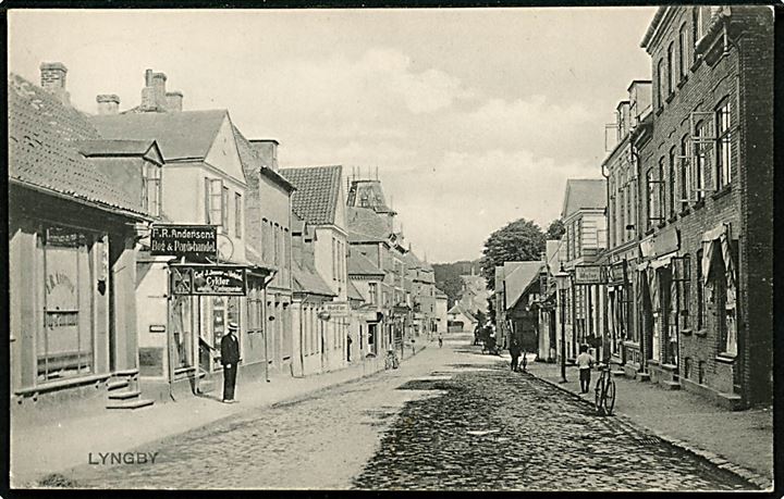 Lyngby. Gadeparti med F.R. Andersens Bog & Papirhandel, Carl J. Jensens Cyklehandler og flere andre. Stenders no. 3793.