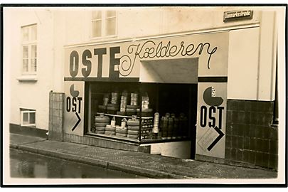 Fredericia. Danmarksstræde med Knud V. Knudsens butik Oste Kælderen. Butikken saboteret i 1944. Ostehandler Knudsen var medlem af DNSAP. Fotokort H. Henriksen, Frederician u/no.