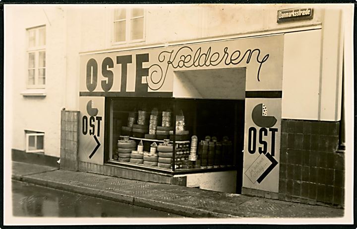 Fredericia. Danmarksstræde med Knud V. Knudsens butik Oste Kælderen. Butikken saboteret i 1944. Ostehandler Knudsen var medlem af DNSAP. Fotokort H. Henriksen, Frederician u/no.