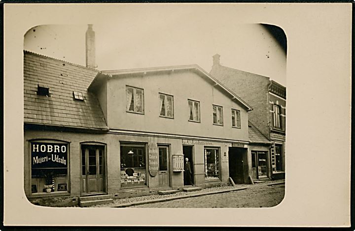 Hobro, bygning med Hobro Mejeri-Udsalg, Jens Fæsters Tobak og Cigarhandel, samt L. C. Lohmann's Pakfarveforretning. Fotokort u/no.